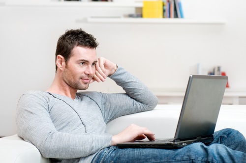 Young Man on a Couch Using a Laptop to Study - Learn to Drive Heavy Equipment Blog