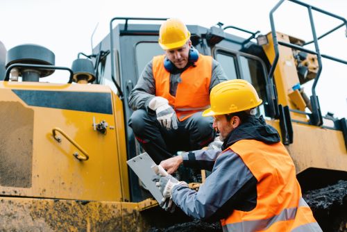 Two construction workers talking in front of heavy equipment.