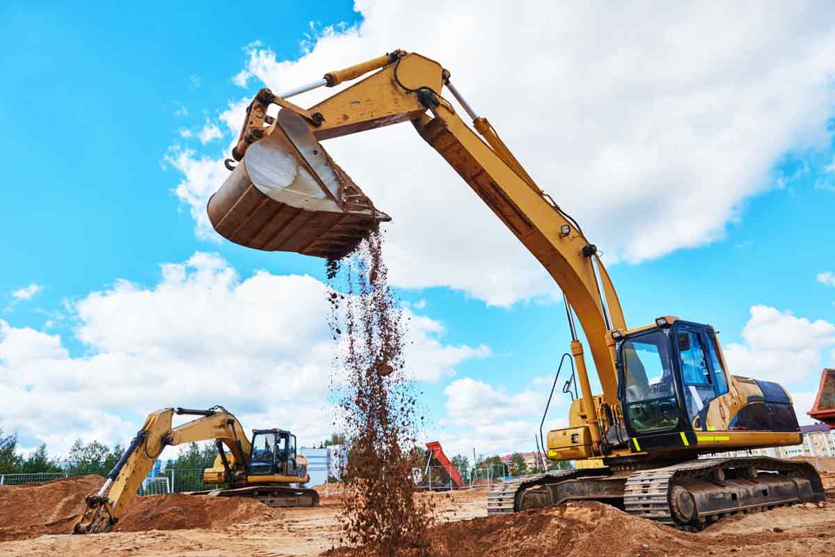 Two construction workers talking in front of heavy equipment.
