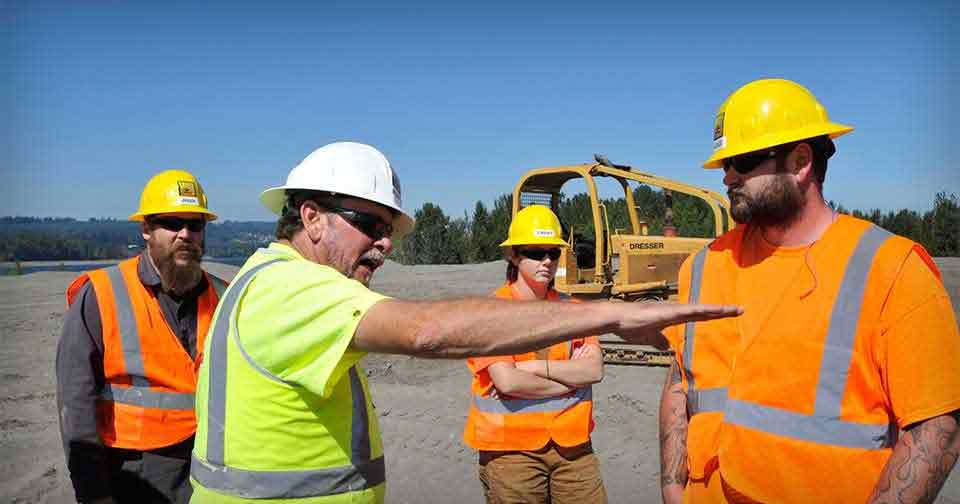 Two construction workers talking in front of heavy equipment.